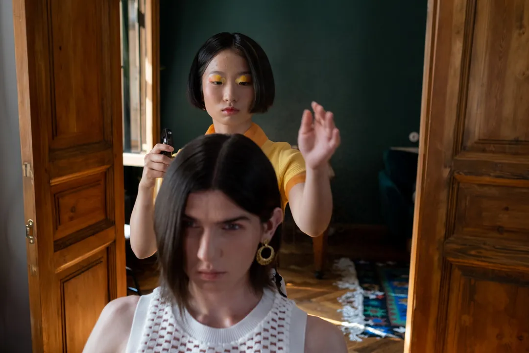A stylist at work in a dark blue salon, seen through open wooden doors