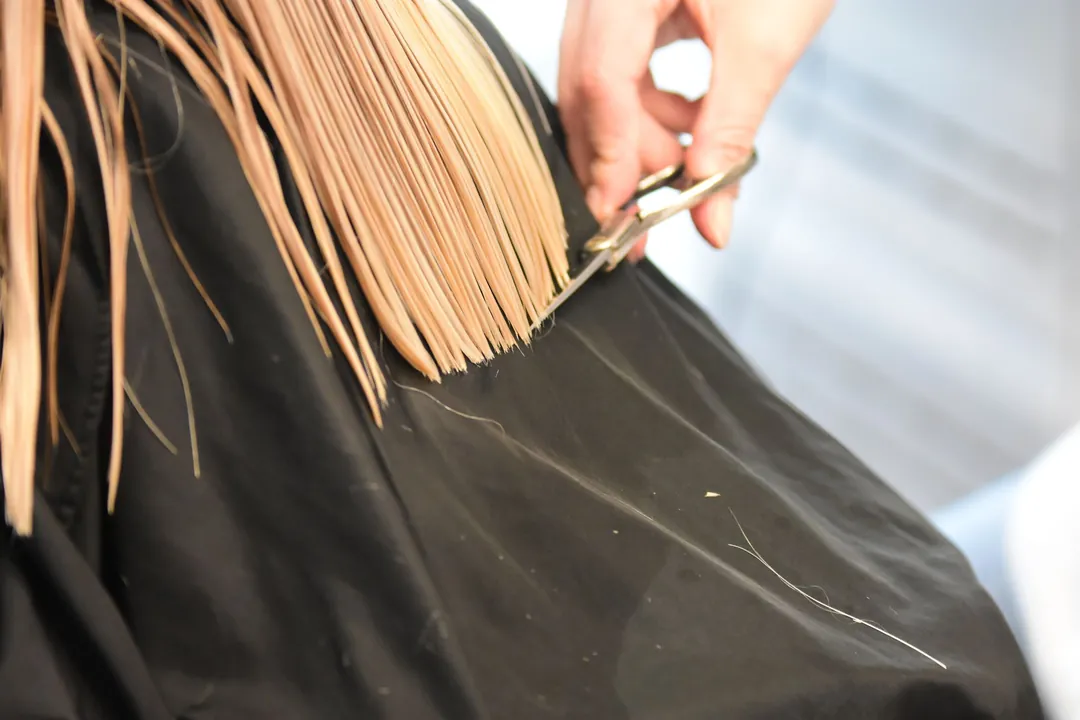 A blunt line being cut through straight blonde hair