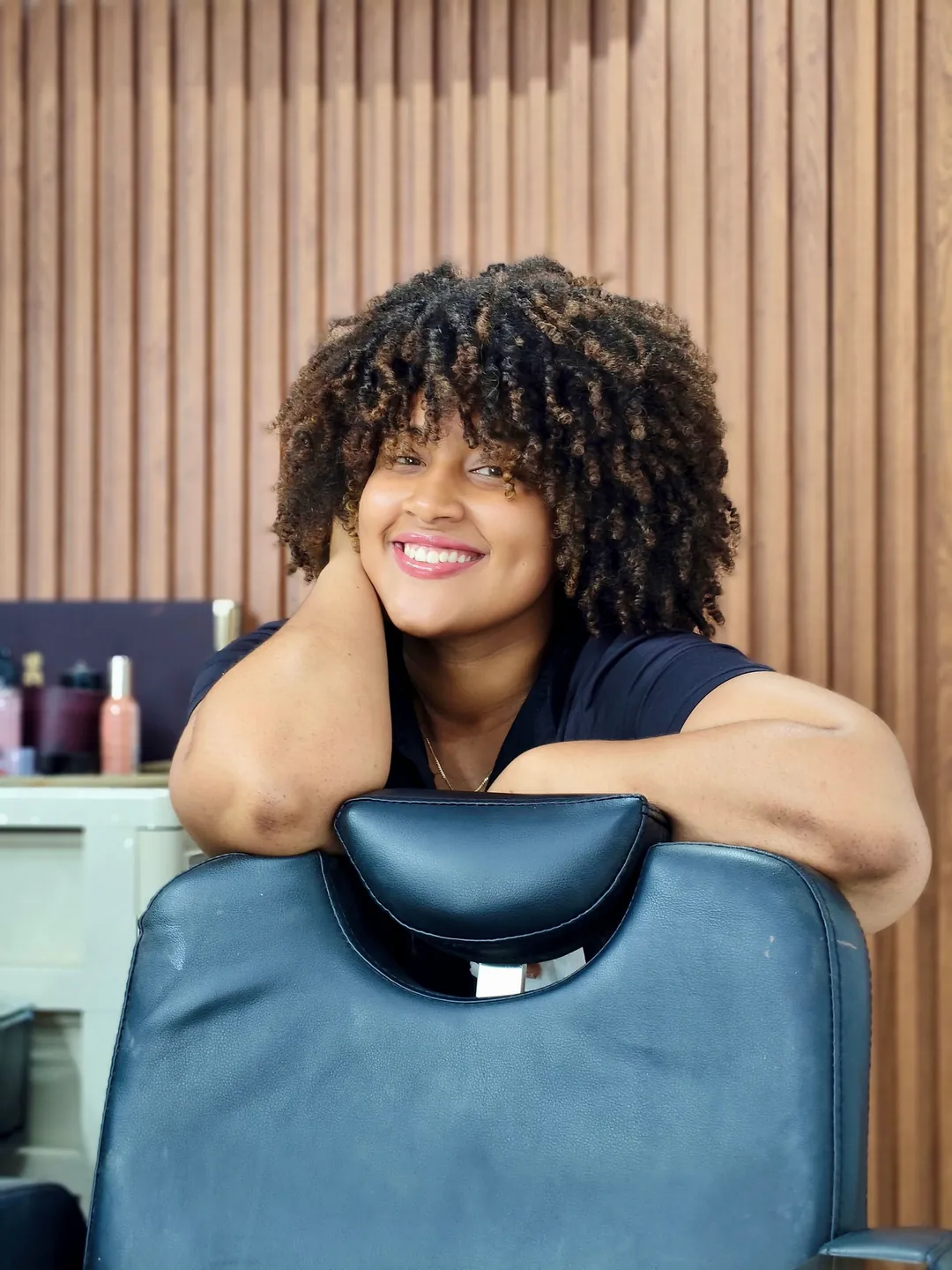 A smiling client with coily hair leaning on a salon chair