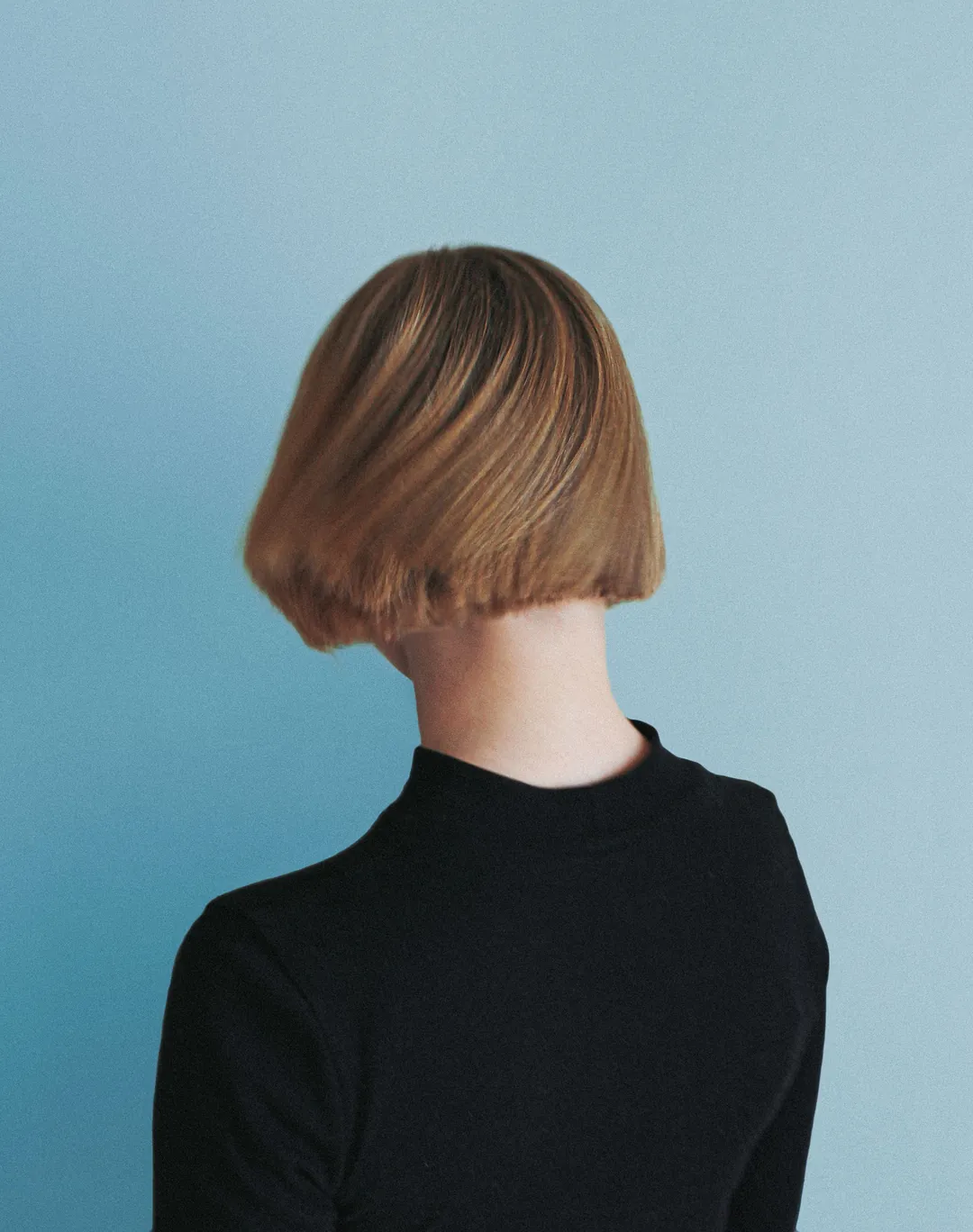 A short blunt bob seen from behind against a blue wall