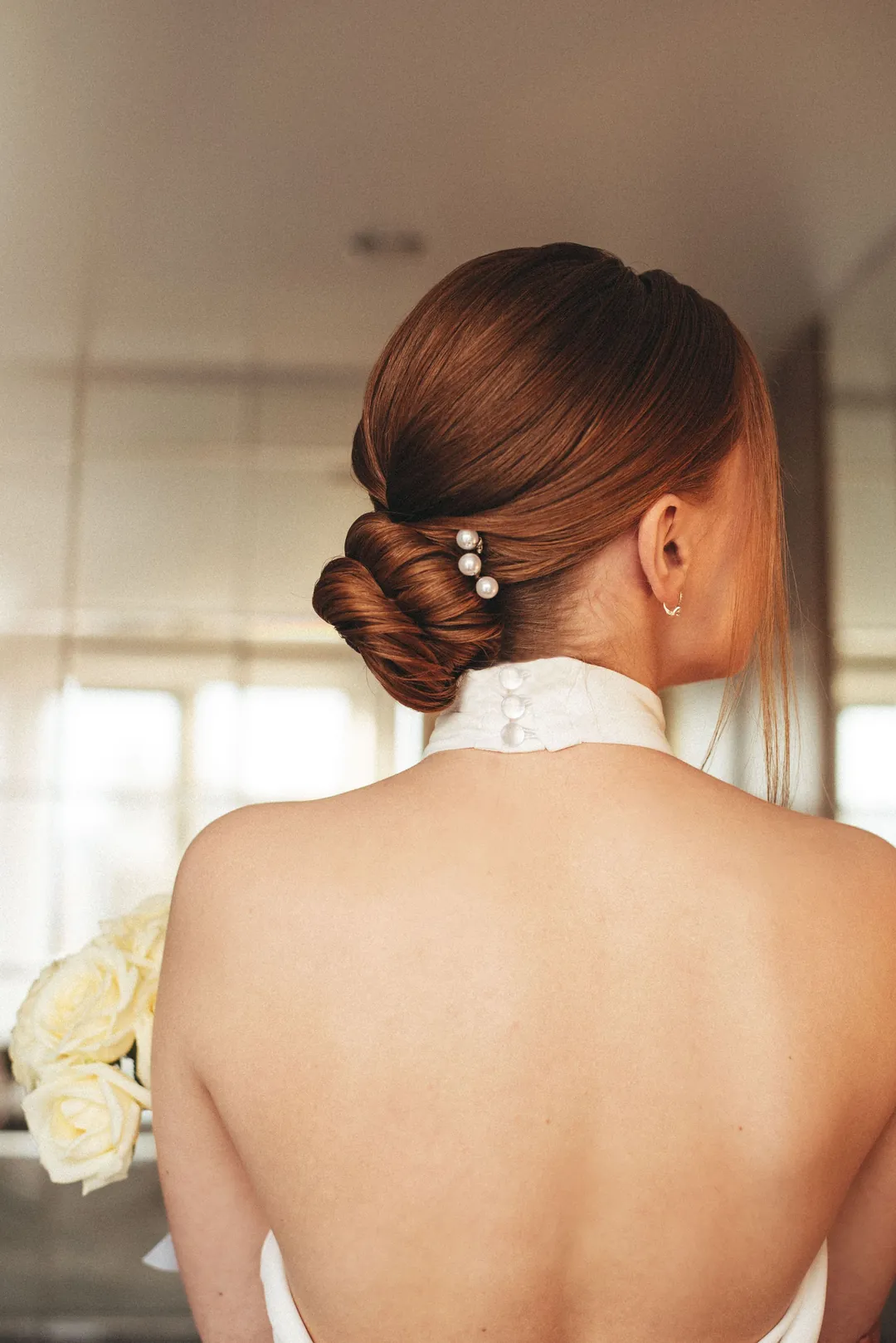 A low twisted bun in copper hair with pearl pins