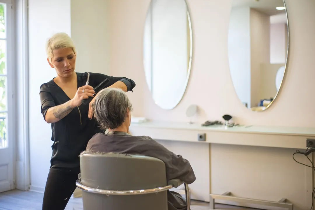 A stylist cutting a client's grey hair in a bright salon