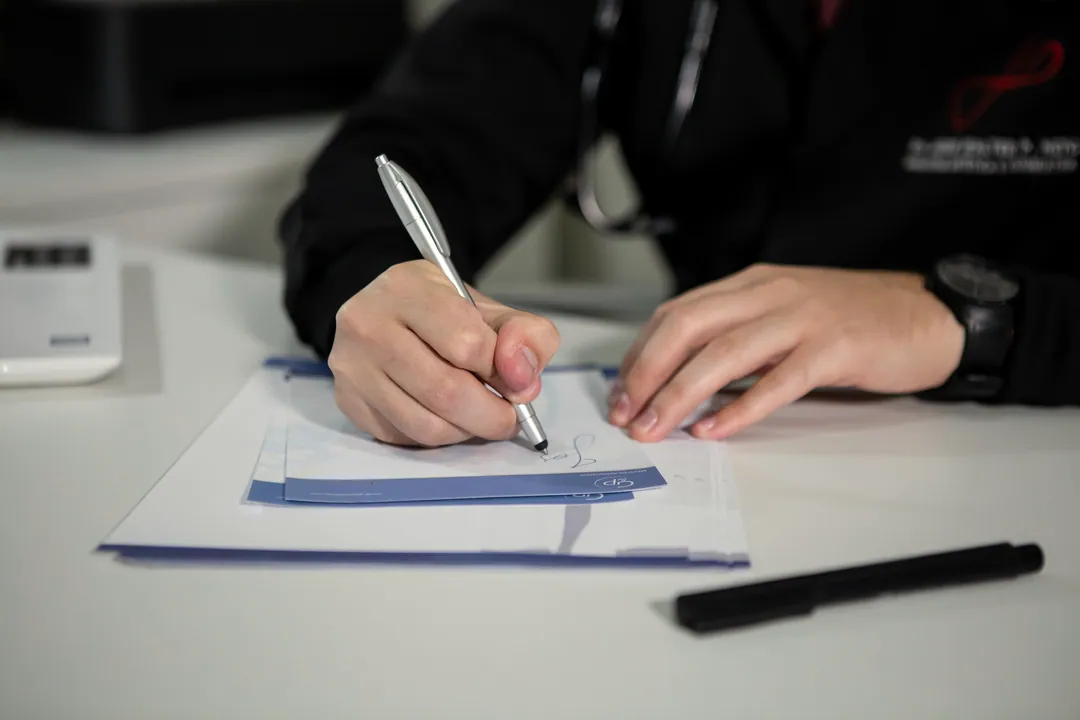 Hands write notes on a clinical form with a pen