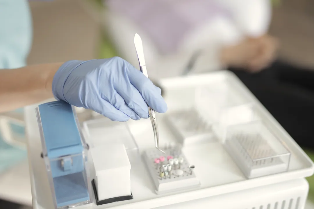 A blue-gloved hand lifts a fine instrument from a sterile tray of small files