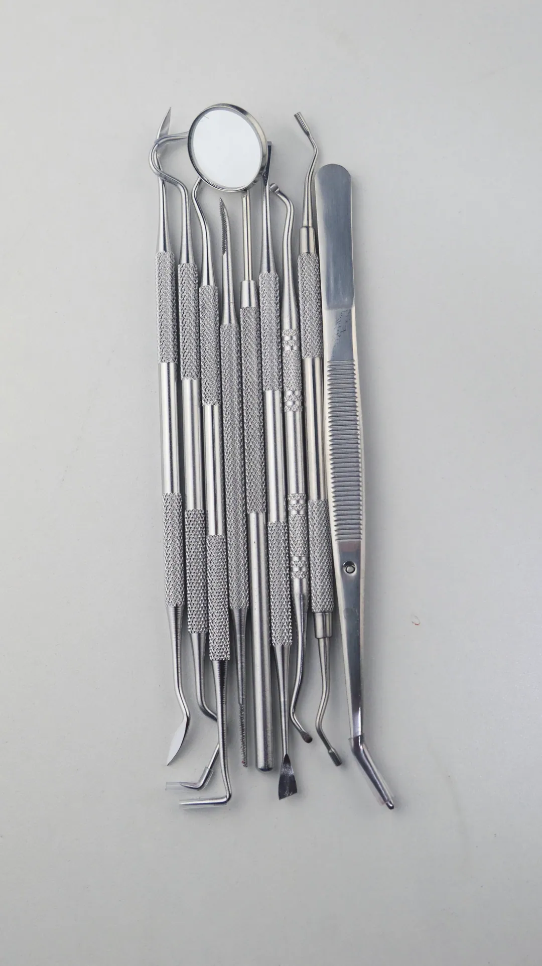 A row of steel dental hand instruments on pale grey