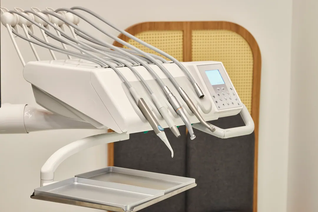 A dental delivery unit with handpieces and an empty tray, against a rattan-panelled wall