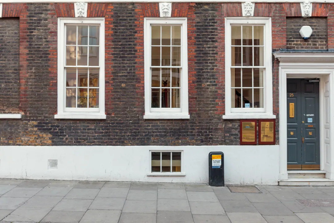 A Georgian brick façade with white sash windows and a plain grey-blue door with a brass plaque