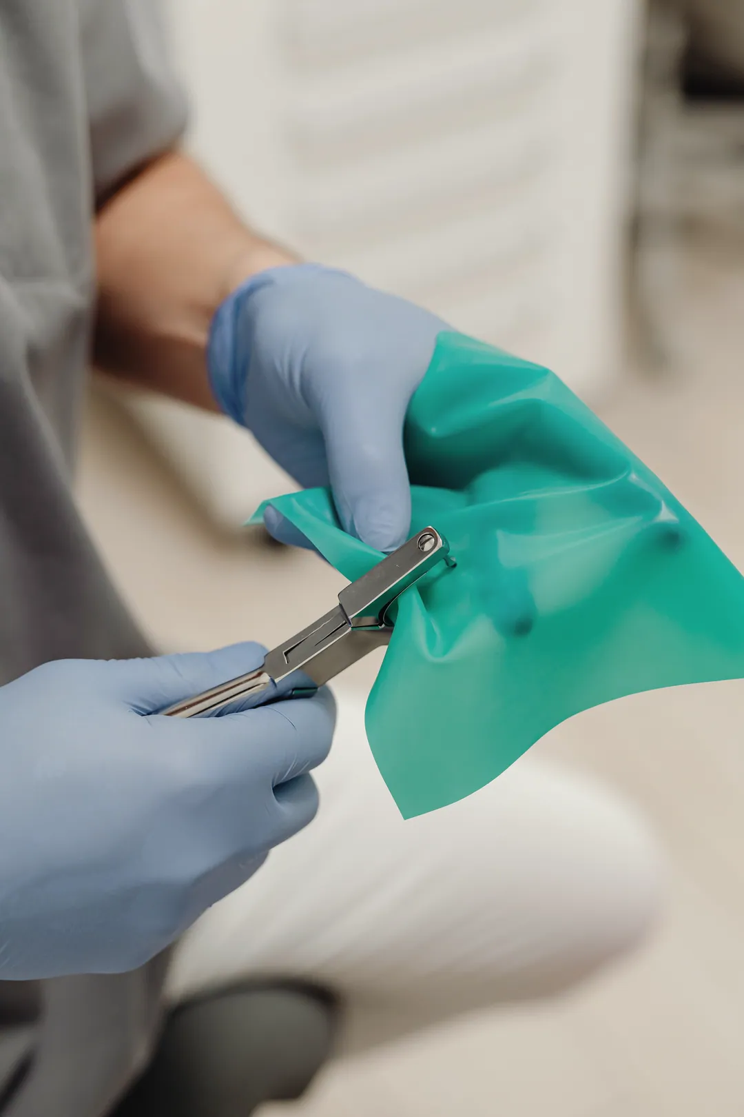 Gloved hands prepare a green rubber dam sheet with a clamp forceps