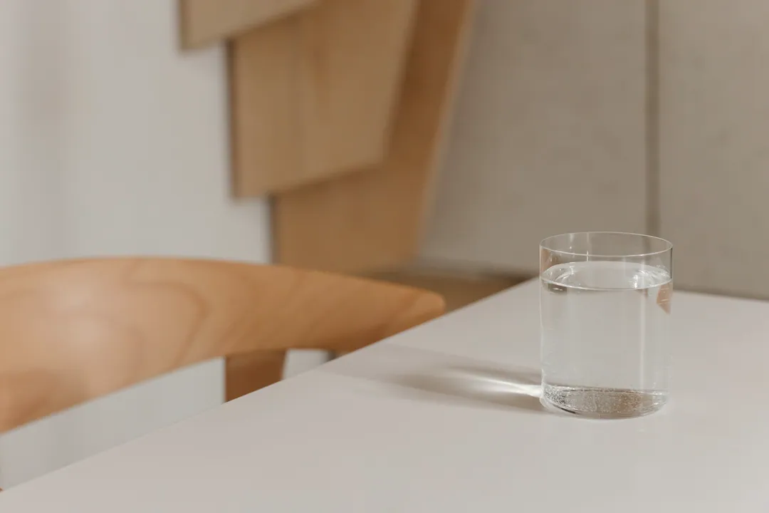 A glass of water on a white table beside a curved plywood chair