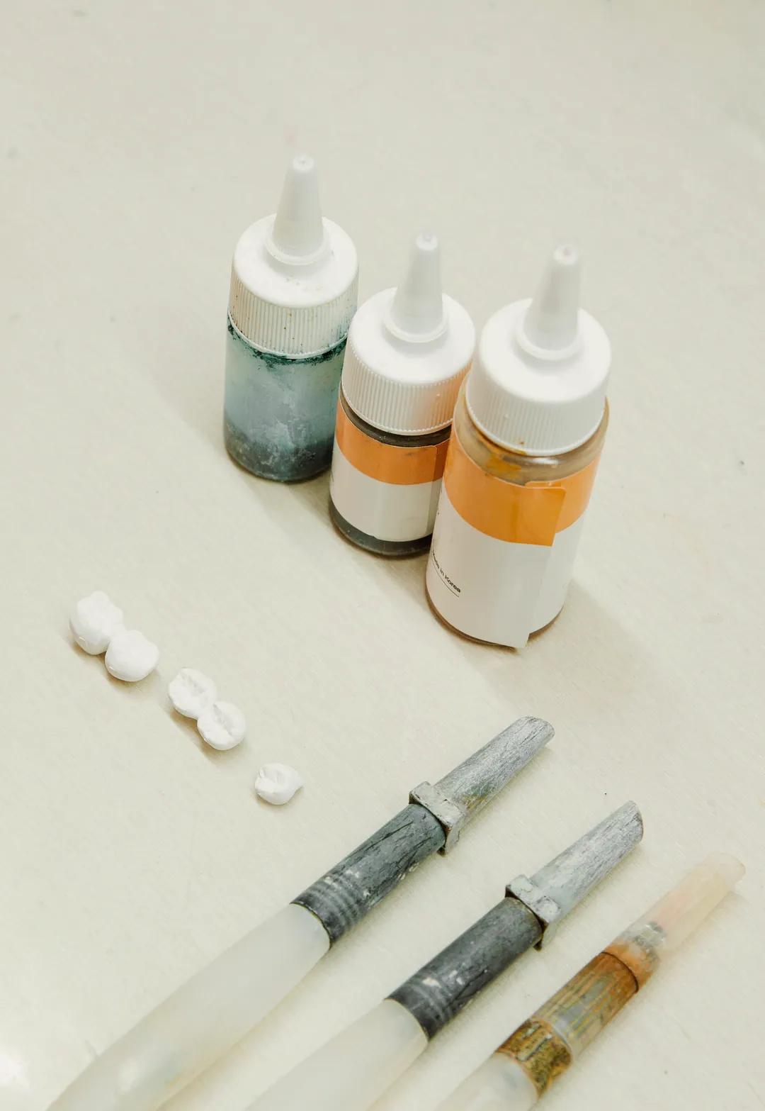 Composite syringes, small pellets and three bottles of material on a white bench