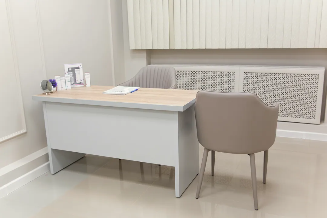 A light oak and white consulting desk with two chairs in an empty white room