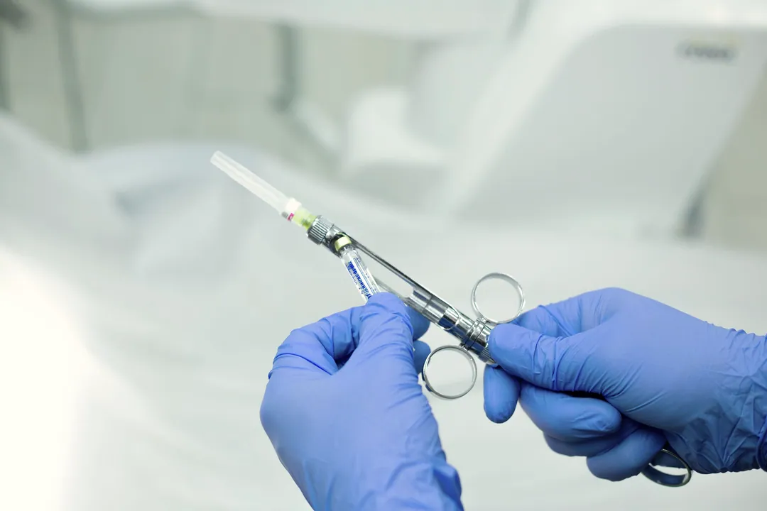 Blue-gloved hands hold a dental cartridge syringe in a bright treatment room