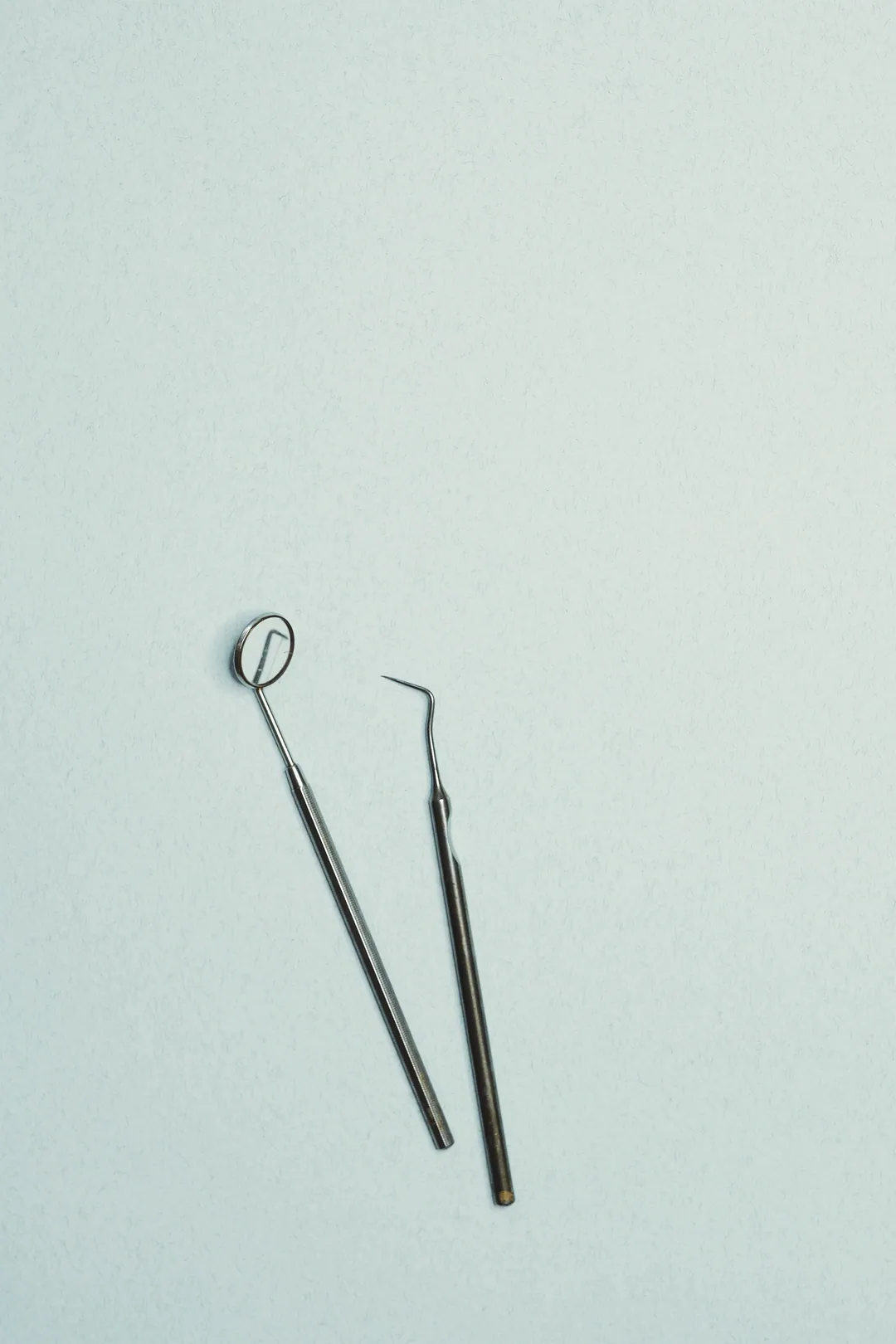 A dental mirror and explorer lie on a pale blue surface