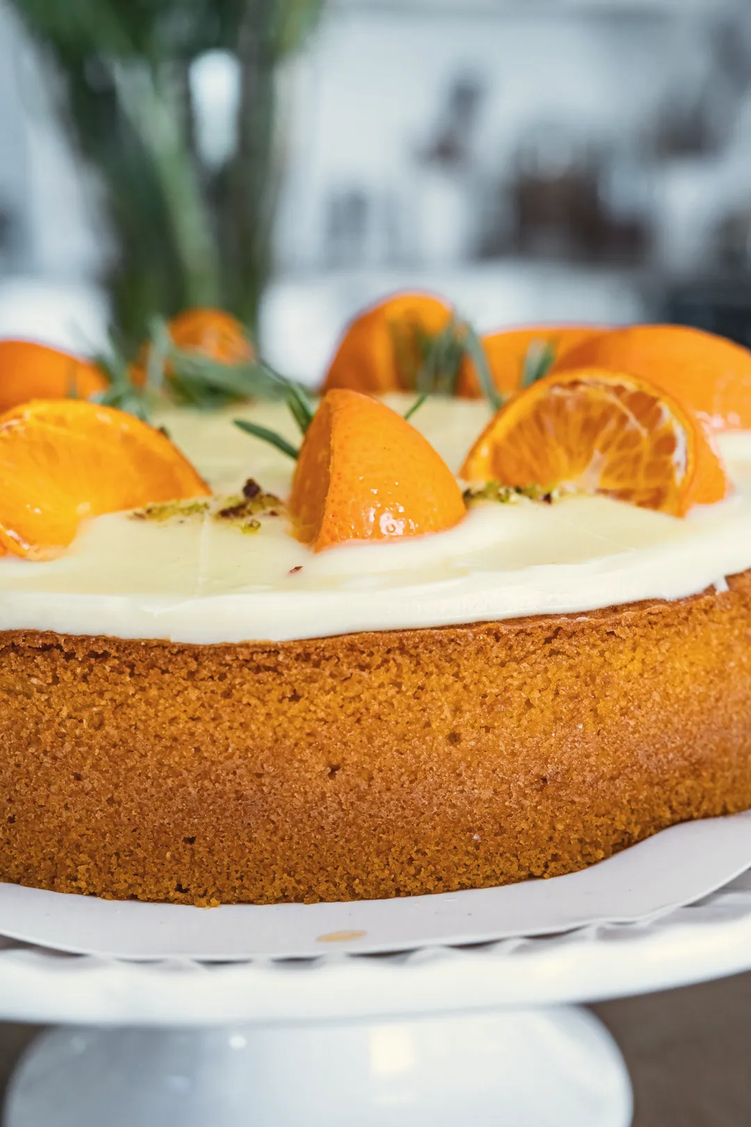 An orange cake on a white stand, topped with orange slices
