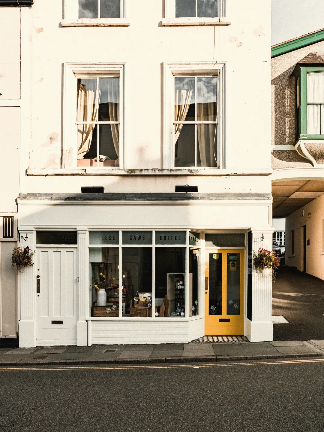 A white corner shop front with a big window and a yellow door