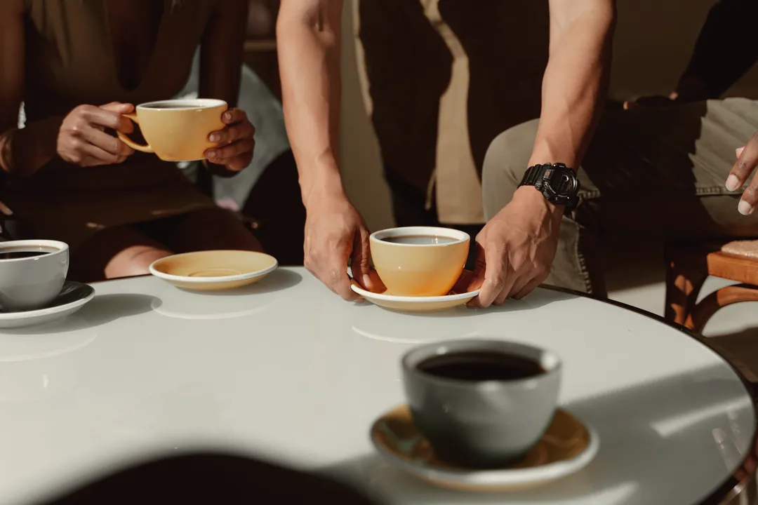 Hands passing cups of coffee across a round café table
