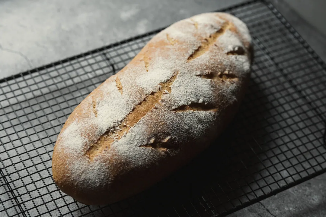 A scored sourdough loaf on a cooling rack