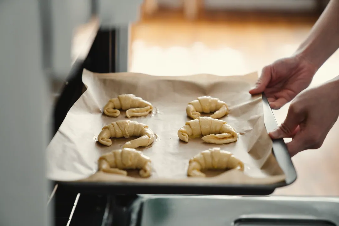 Hands sliding a tray of unbaked croissants into the oven