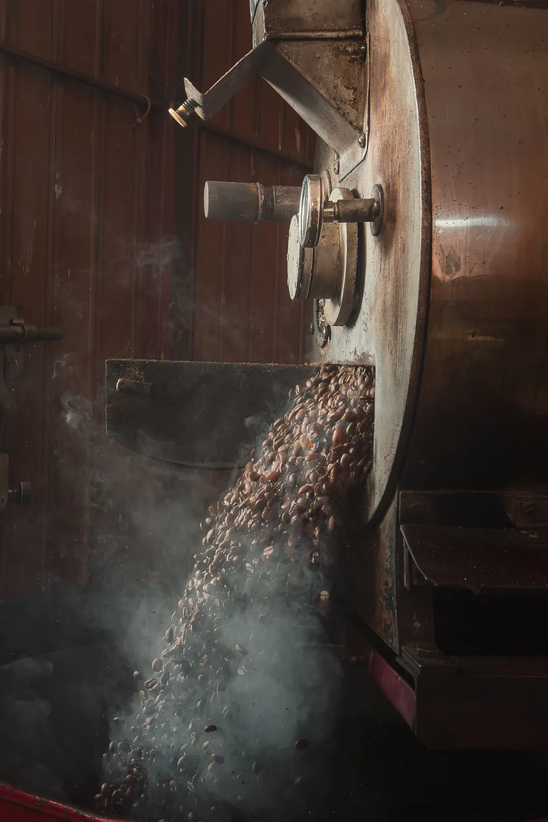 Roasted beans pouring out of the drum into the cooling tray, with smoke