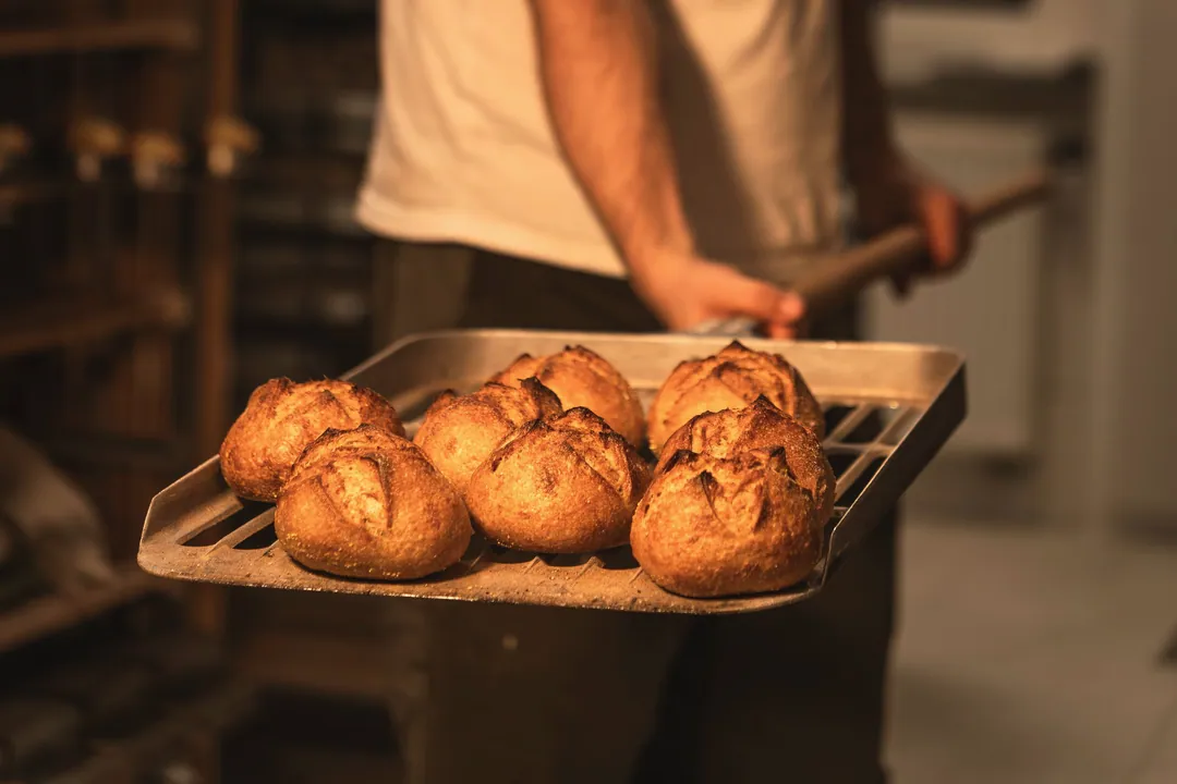 A baker carrying a tray of fresh round loaves