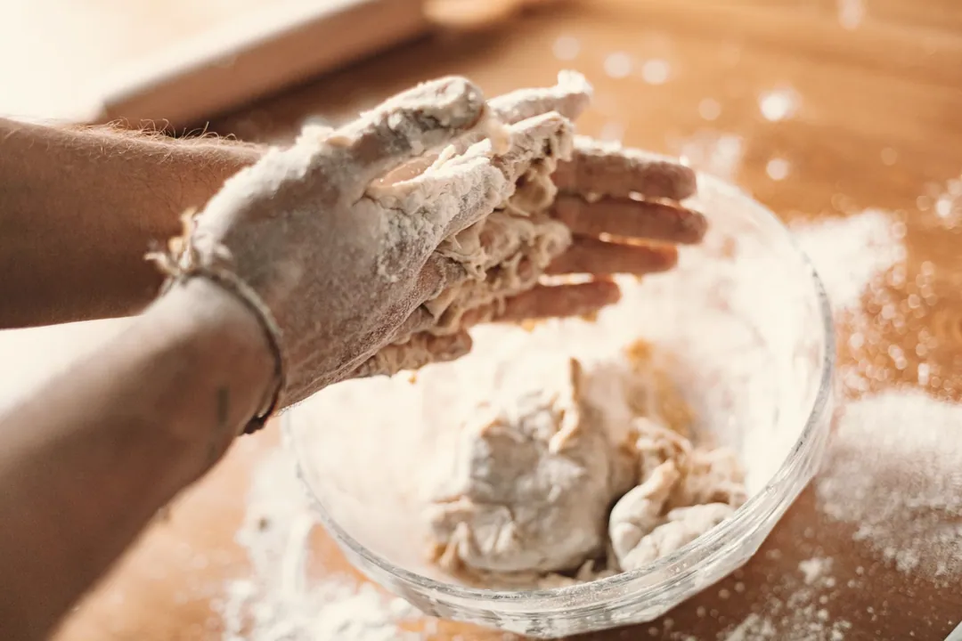 Floury hands working dough in a glass bowl