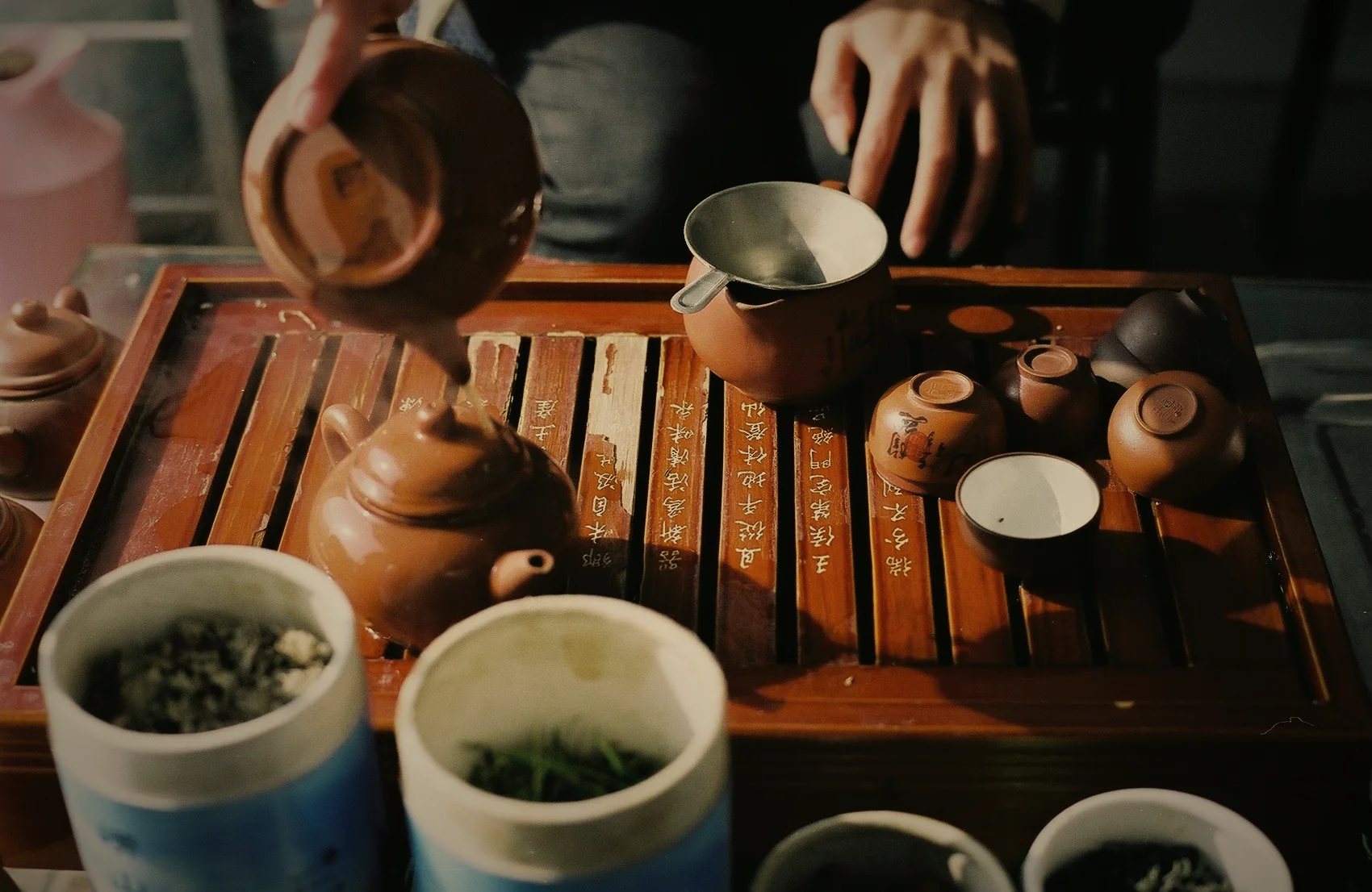 A host pouring gongfu tea from a small pot into cups on a slatted tea tray