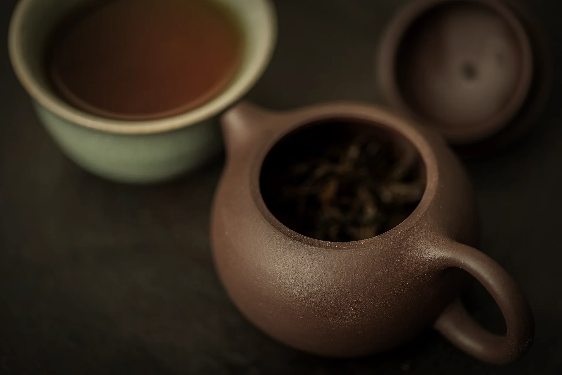 A clay teapot and a cup of dark tea on a dark table