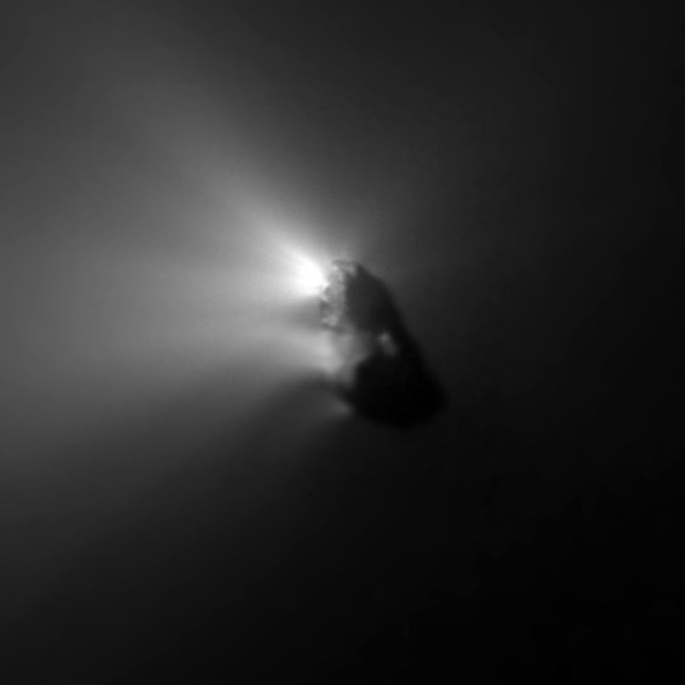 Grainy close-up of a dark, elongated nucleus with bright jets of gas on its sunward side.