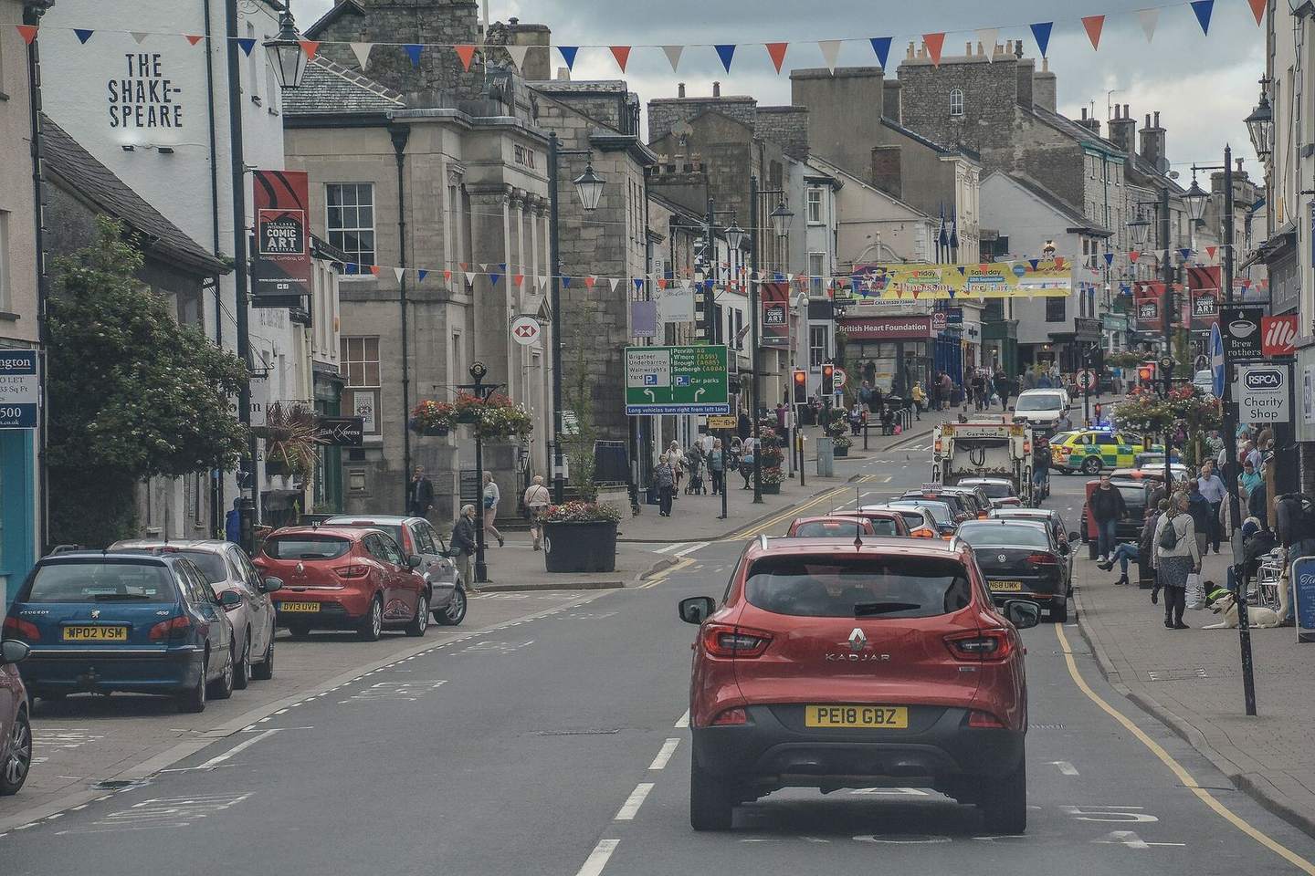 Highgate, Kendal's main street, with grey stone shop fronts and traffic on a summer day