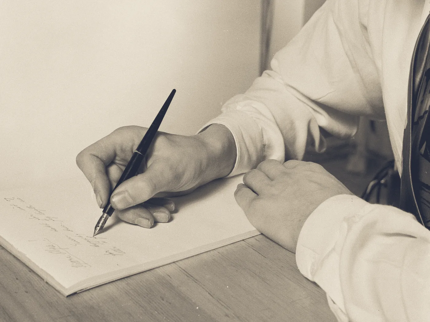 A hand writing out a fountain pen on a pad of paper, the other hand holding the pad flat