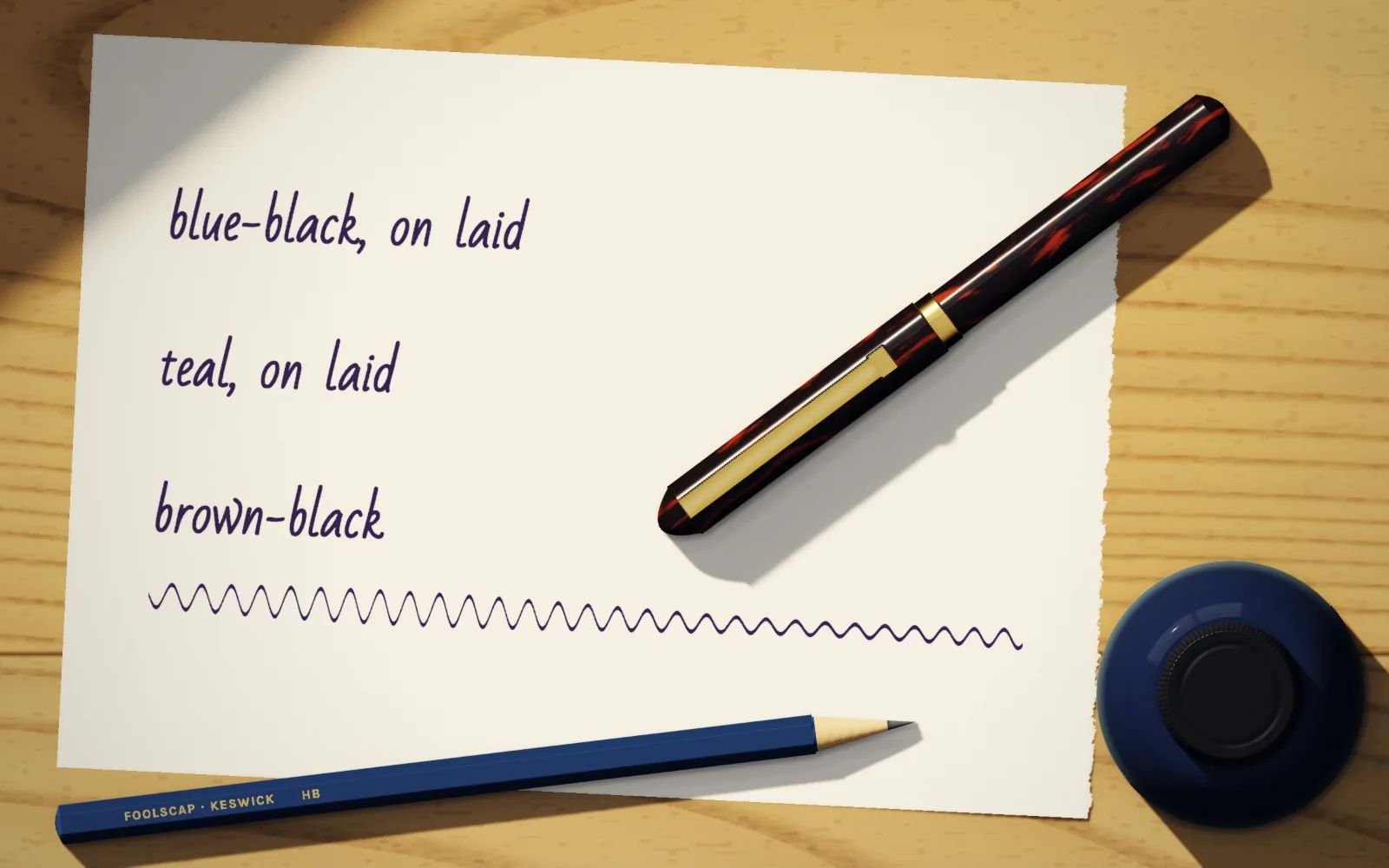 Three inks written out on laid paper, an ebonite fountain pen, a pencil and a bottle of ink on the oak counter