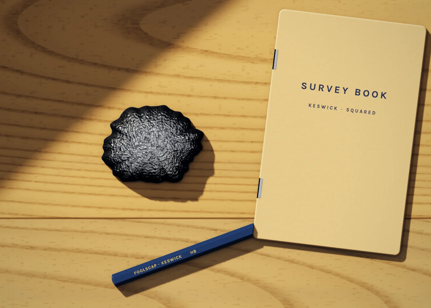 A lump of graphite beside a blue Foolscap pencil and a squared pocket survey book on the counter