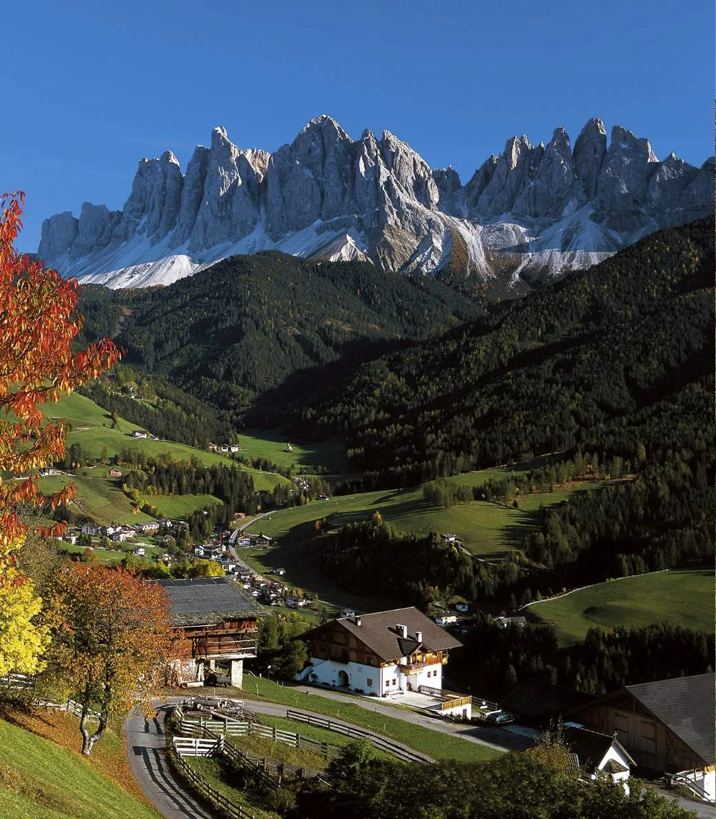 The road into Villnöss between autumn trees, a few houses, and the Geisler at the head of the valley.