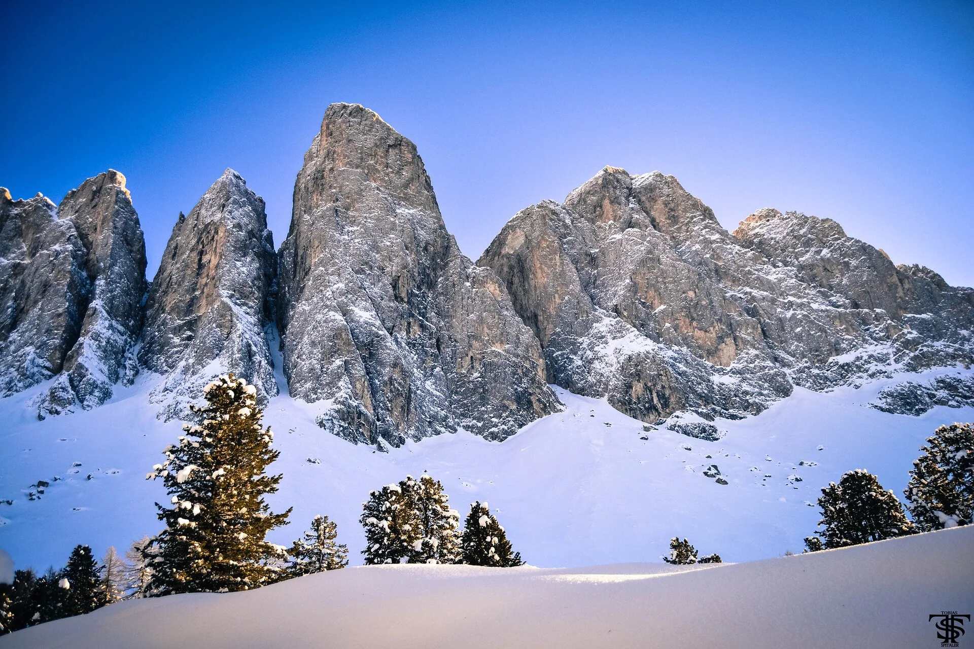 The Geisler peaks deep in snow under a blue sky.