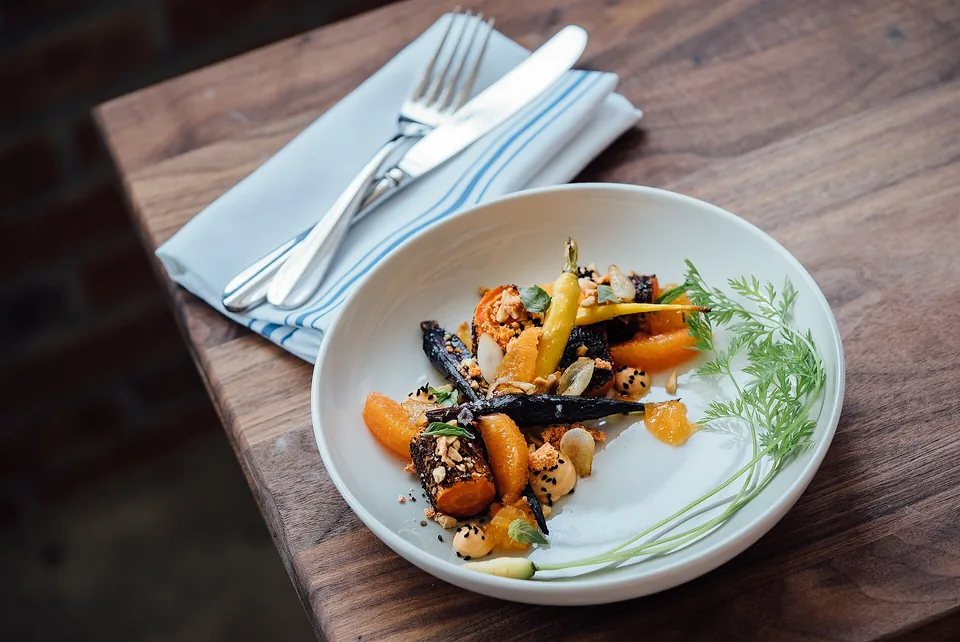 Roast carrots with herbs on a white plate on a dark wooden table