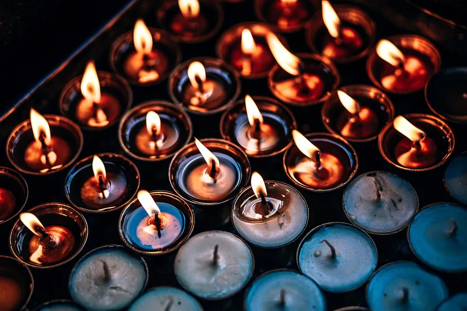 Rows of tea lights in a dark tray, some burning, some burnt out