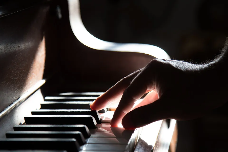 A hand on the keys of an upright piano, lit from the side in a dark room