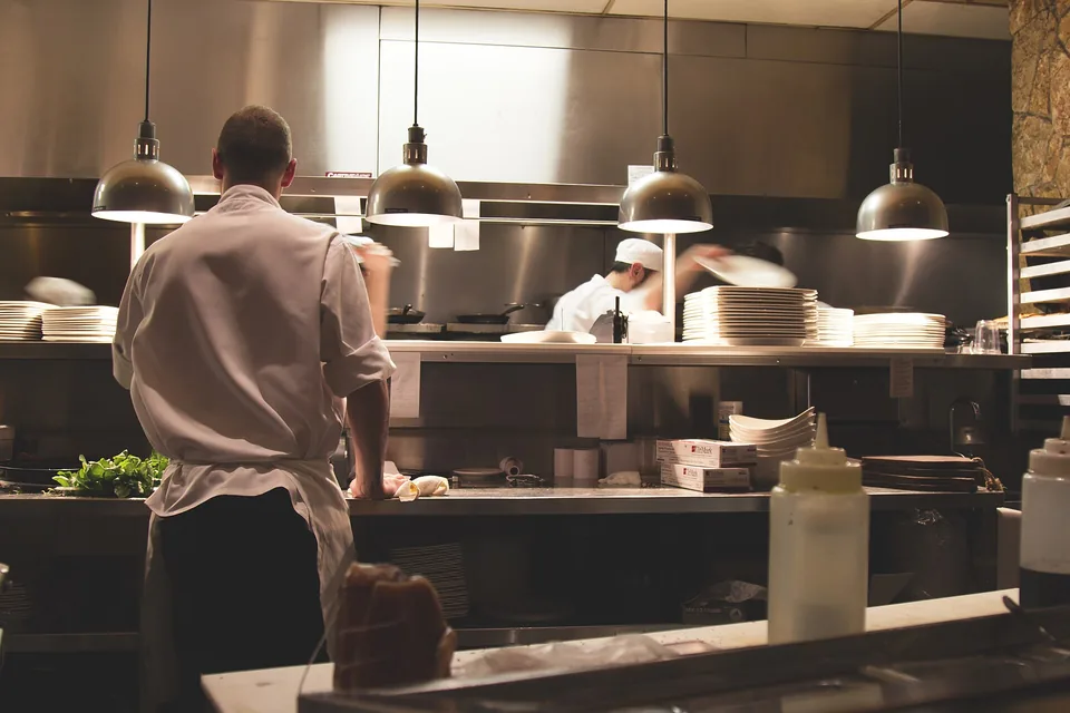 Cooks working at the pass under a row of pendant lamps