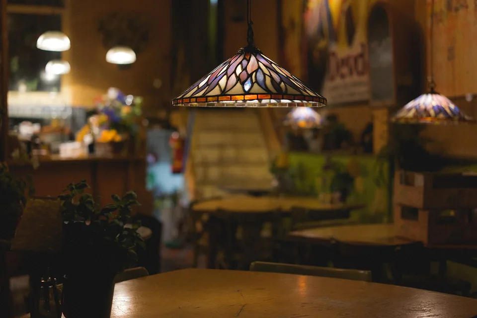 A stained-glass lamp low over a wooden table in a dim room, a second lamp further back