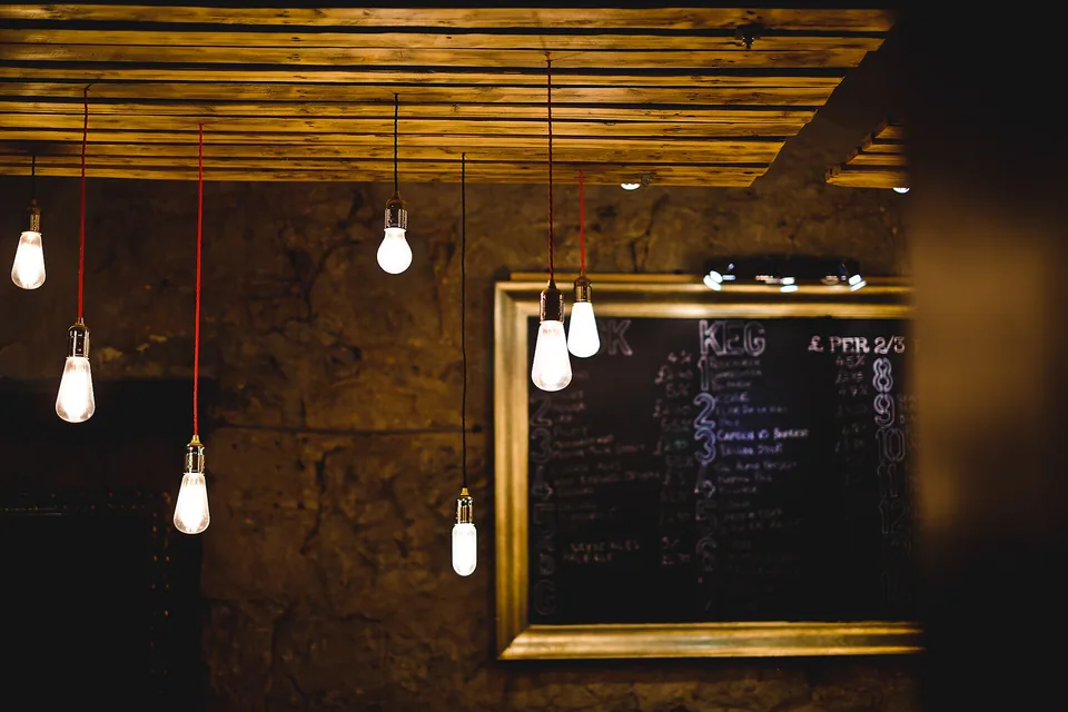 Bare filament bulbs on red flex hanging from a timber ceiling, a chalk board on a stone wall behind