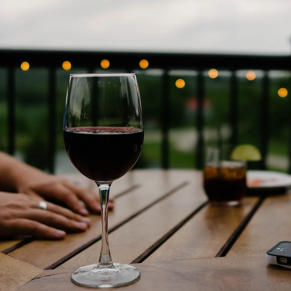 A glass of red wine on a wooden table, string lights blurred behind