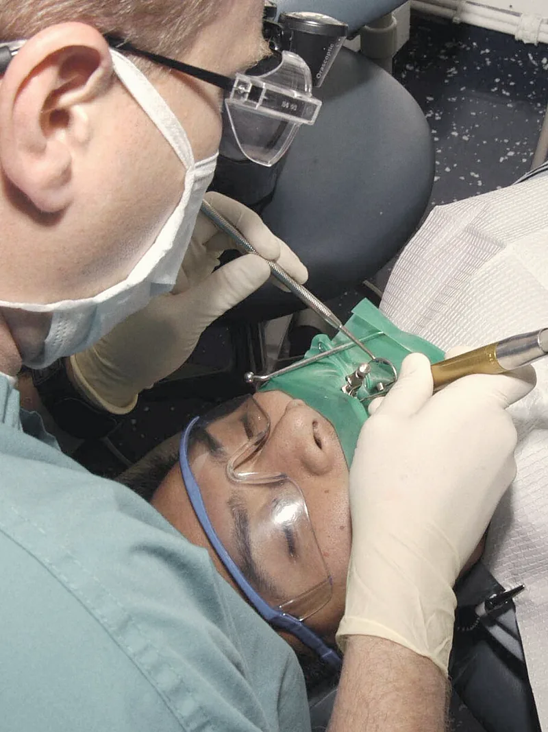 A dentist wearing magnifying loupes works on a patient's tooth