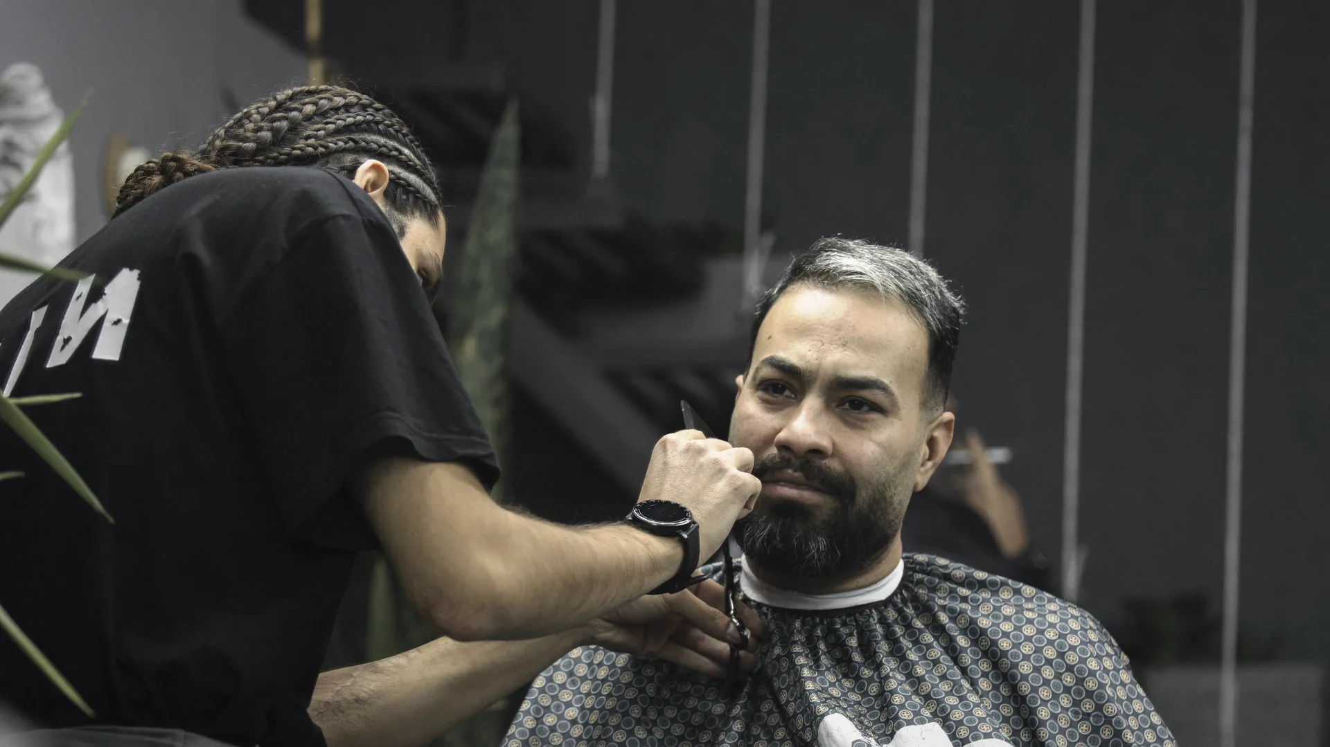 A barber shaping a client's beard with scissors