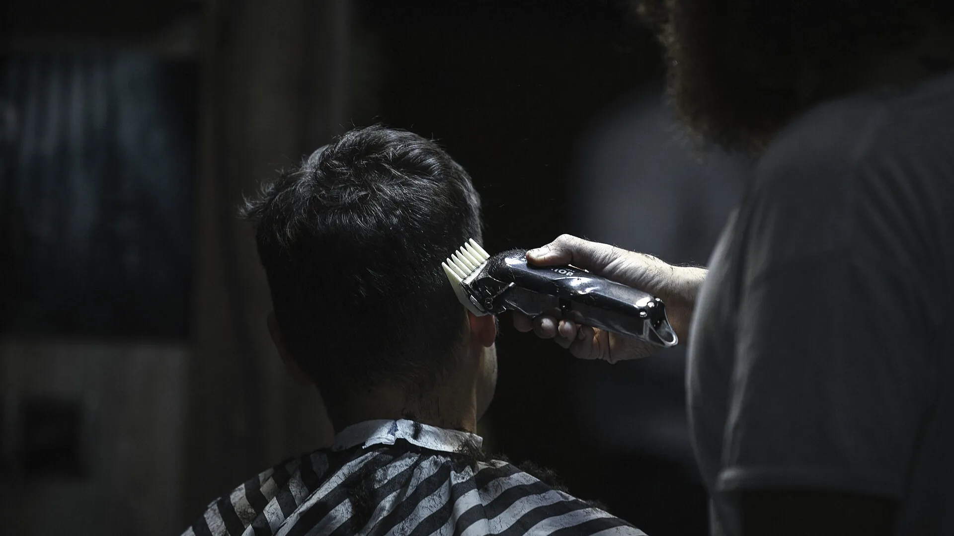A barber running clippers with a guard up the side of a client's head
