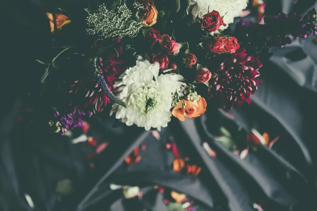 White and burgundy dahlias, orange roses and seed heads on dark cloth