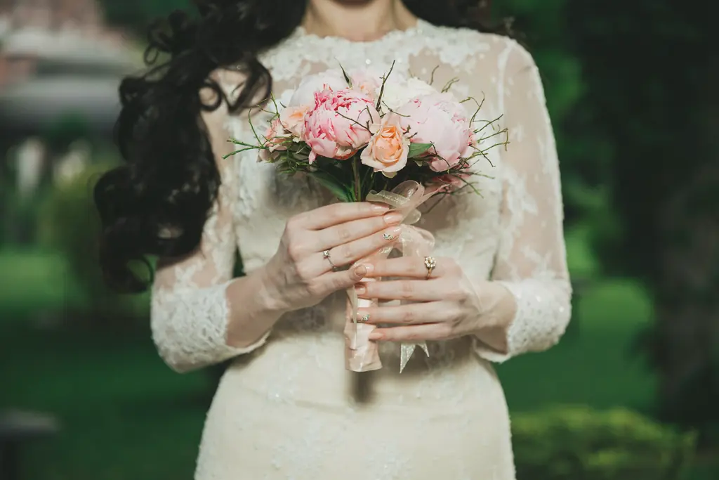 A bride in lace holding a small bouquet of peach roses