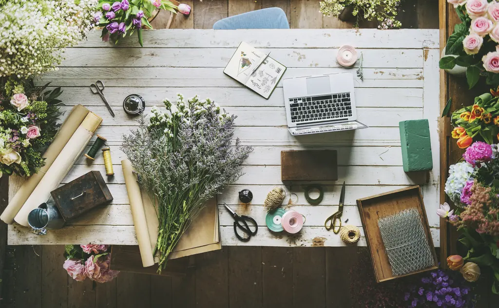 A florist's bench from above: scissors, rolls of paper, lavender, ribbon and a laptop