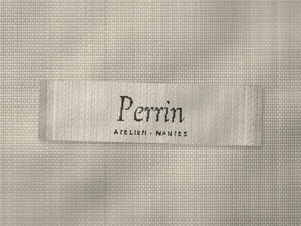 Woven label reading Perrin, Atelier, Nantes, black italic on cream, stitched onto white shirting