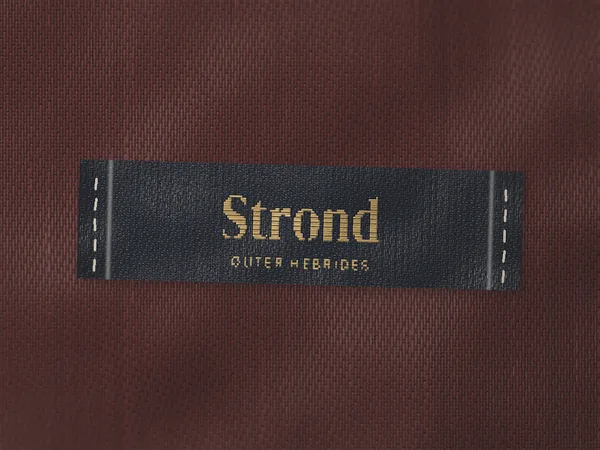 Woven label reading Strond, Outer Hebrides, in gold on navy, stitched onto a coat lining