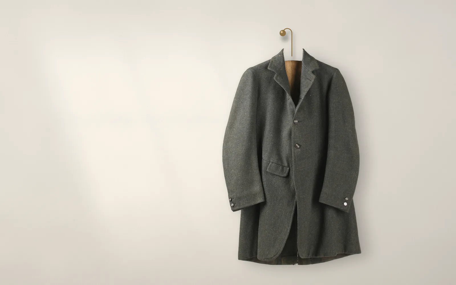 No. 06, the loden jacket in green loden, hanging from a brass peg on the shop's paper-coloured wall in afternoon light